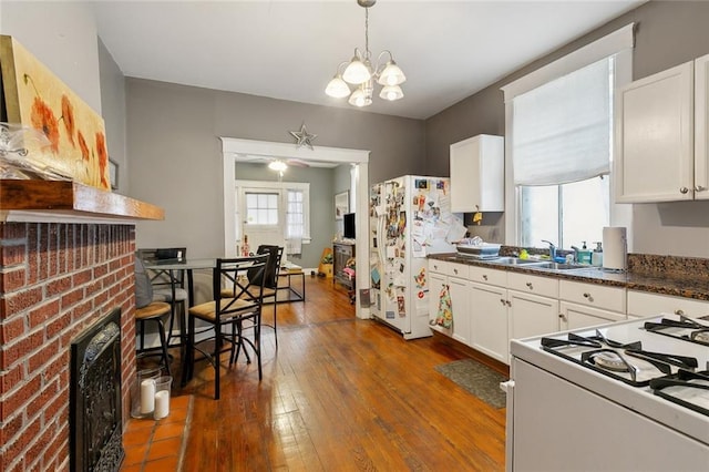 kitchen featuring a sink, hardwood / wood-style floors, white cabinetry, white appliances, and a brick fireplace