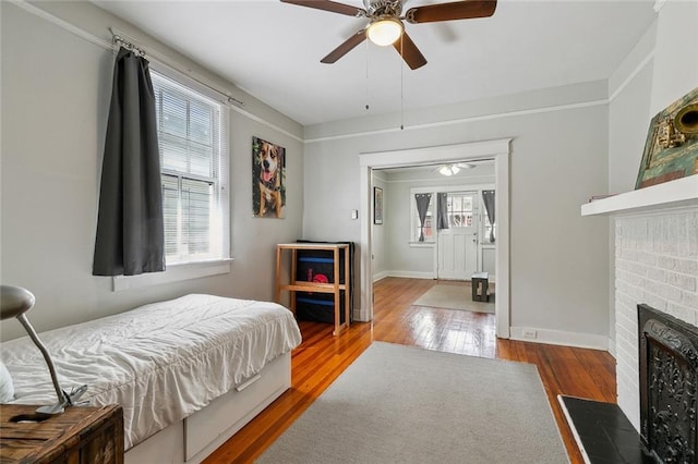 bedroom featuring hardwood / wood-style floors, a fireplace, baseboards, and a ceiling fan