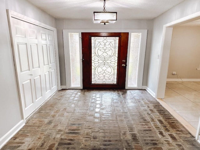 foyer featuring brick floor and baseboards