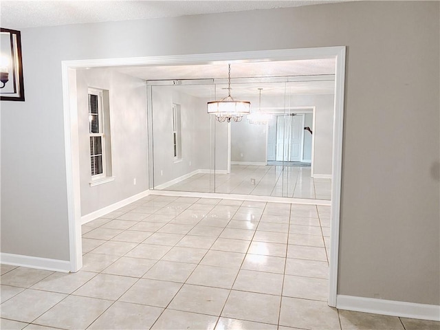 interior space featuring light tile patterned floors, a notable chandelier, a textured ceiling, and baseboards