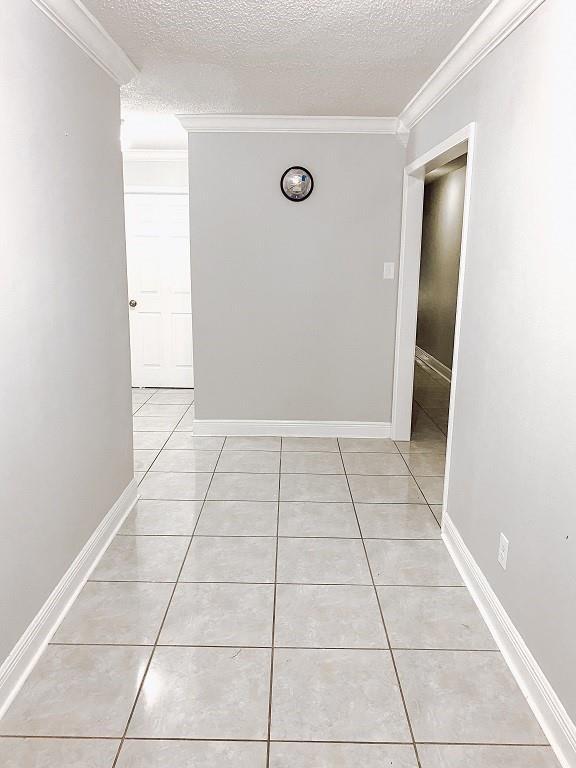 hallway featuring light tile patterned floors, baseboards, a textured ceiling, and ornamental molding