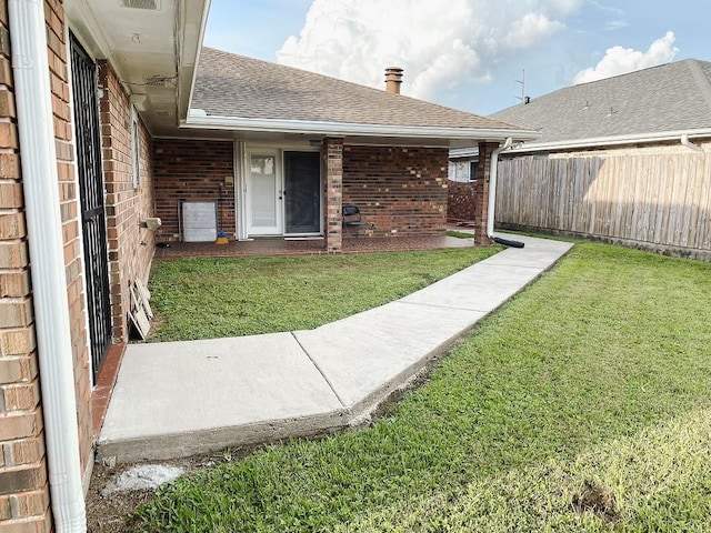 exterior space with a yard, brick siding, a shingled roof, and fence