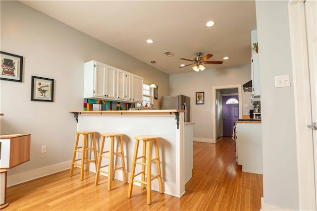 kitchen featuring visible vents, freestanding refrigerator, a peninsula, a breakfast bar area, and ceiling fan