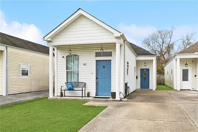 shotgun-style home featuring a front lawn, covered porch, driveway, and a shingled roof