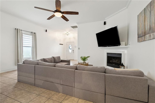 living room with visible vents, crown molding, light tile patterned floors, a fireplace, and a ceiling fan