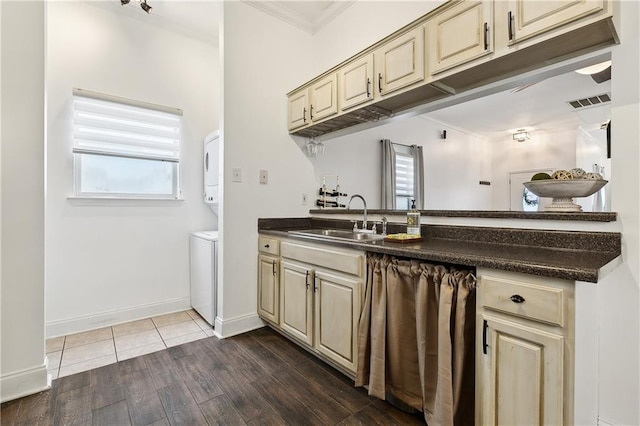 kitchen with dark countertops, cream cabinets, stacked washing maching and dryer, dark wood-style floors, and a sink