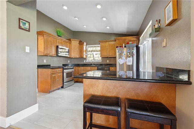 kitchen with a kitchen bar, vaulted ceiling, appliances with stainless steel finishes, a peninsula, and brown cabinetry