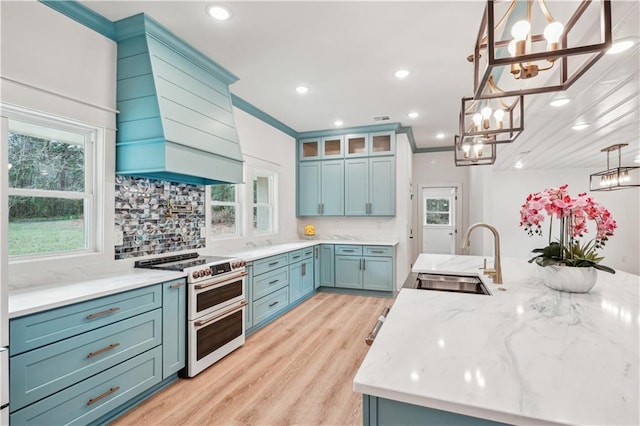 kitchen with a sink, double oven range, a chandelier, light wood-style flooring, and custom range hood
