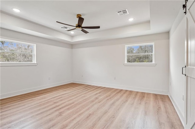 empty room featuring plenty of natural light, visible vents, and a raised ceiling