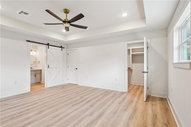 unfurnished bedroom with visible vents, light wood-style floors, a raised ceiling, and a barn door