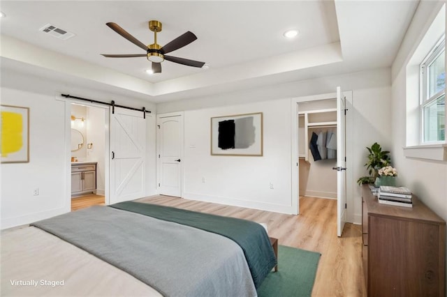 bedroom featuring a spacious closet, a barn door, visible vents, and a raised ceiling