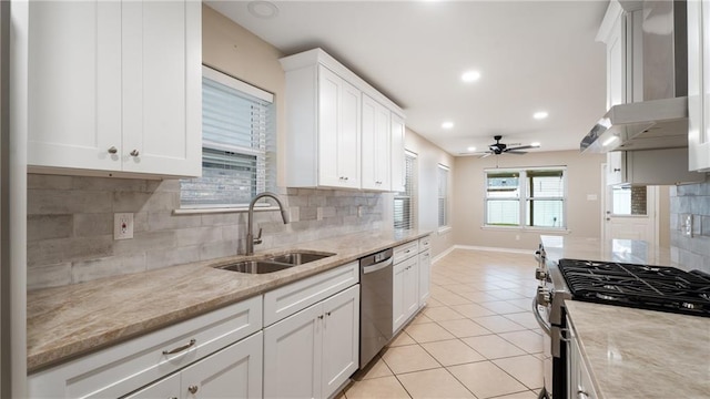 kitchen with a ceiling fan, a sink, appliances with stainless steel finishes, wall chimney exhaust hood, and light tile patterned floors