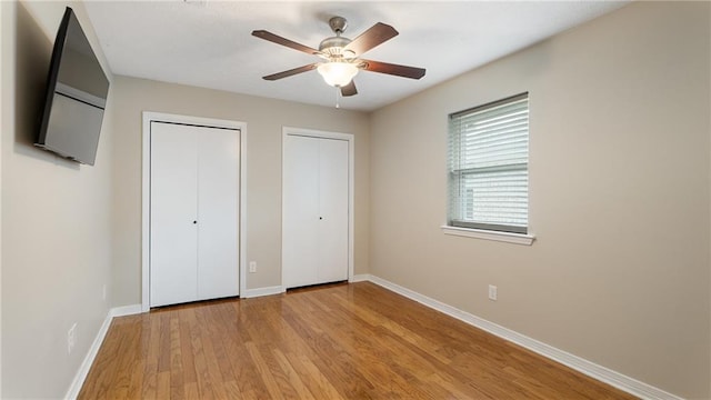 unfurnished bedroom with a ceiling fan, light wood-style floors, baseboards, and two closets