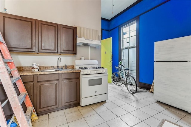 kitchen featuring under cabinet range hood, a sink, white appliances, light countertops, and light tile patterned floors