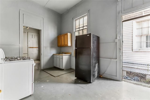 kitchen featuring concrete flooring, white gas range oven, and freestanding refrigerator