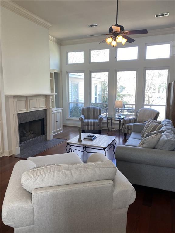 living area with visible vents, dark wood-style flooring, ornamental molding, and a ceiling fan