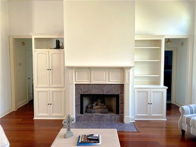 living room with dark wood finished floors, a tiled fireplace, and baseboards