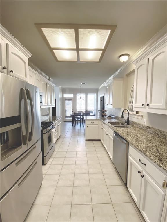 kitchen featuring ornamental molding, appliances with stainless steel finishes, a peninsula, light tile patterned flooring, and a sink