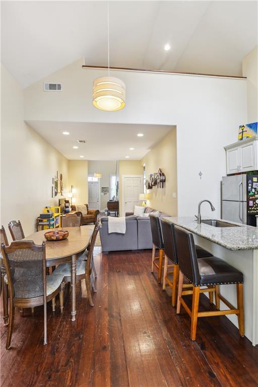 dining room with dark wood-type flooring, recessed lighting, visible vents, and vaulted ceiling