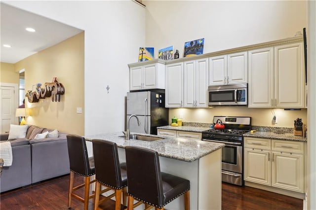 kitchen with a kitchen bar, dark wood-type flooring, appliances with stainless steel finishes, and a sink