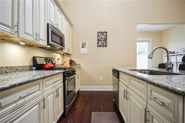 kitchen with a sink, baseboards, light stone counters, appliances with stainless steel finishes, and dark wood-style flooring