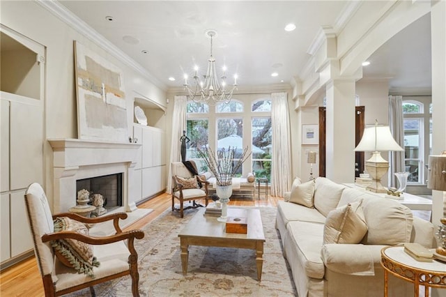 living area with a chandelier, a fireplace with raised hearth, light wood-type flooring, and ornamental molding