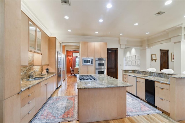 kitchen featuring visible vents, light brown cabinets, a kitchen island, built in appliances, and a sink