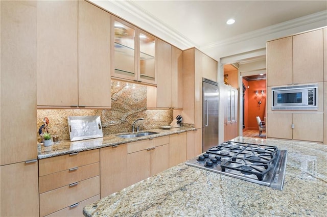 kitchen with light brown cabinetry, built in appliances, ornamental molding, light stone counters, and a sink