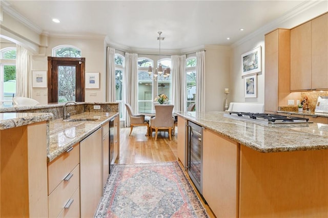 kitchen with a healthy amount of sunlight, beverage cooler, stainless steel gas cooktop, light brown cabinetry, and a sink