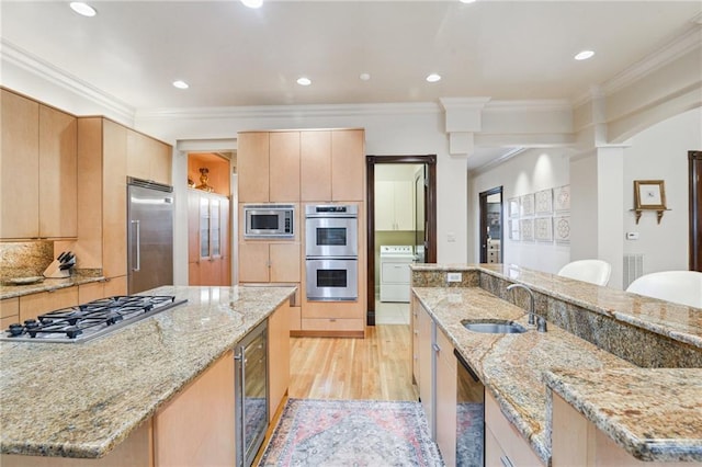 kitchen with beverage cooler, a sink, light wood-style floors, built in appliances, and washer / dryer