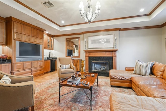 living area featuring visible vents, light wood-type flooring, a fireplace, a notable chandelier, and a raised ceiling