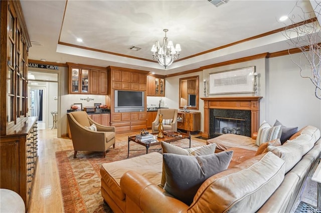 living room with crown molding, a chandelier, a tray ceiling, a premium fireplace, and light wood-style floors