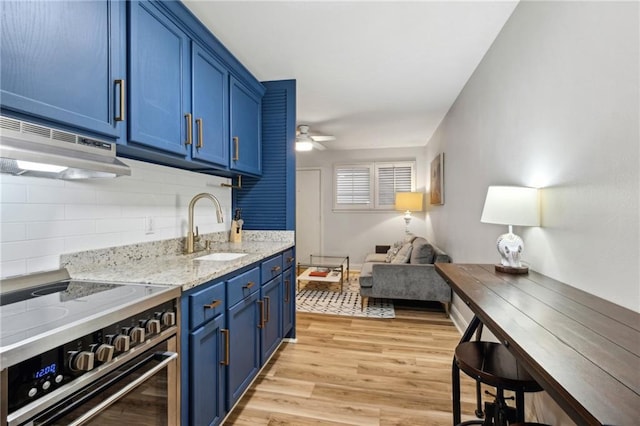 kitchen with a sink, range with electric cooktop, light wood-style floors, under cabinet range hood, and blue cabinets