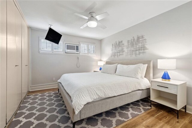 bedroom with baseboards, wood finished floors, and a wall mounted AC