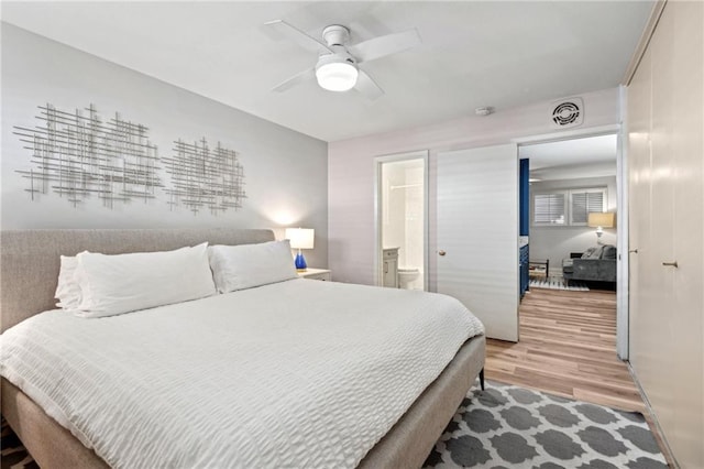 bedroom with visible vents, light wood-style floors, ensuite bathroom, and a ceiling fan