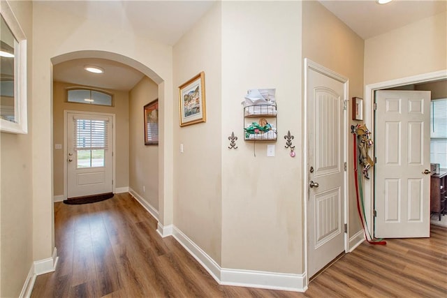 foyer entrance featuring wood finished floors, arched walkways, and baseboards