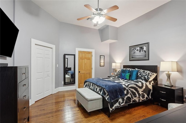 bedroom featuring a closet, baseboards, hardwood / wood-style floors, ceiling fan, and high vaulted ceiling