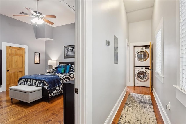 bedroom with baseboards, electric panel, stacked washing maching and dryer, high vaulted ceiling, and wood finished floors