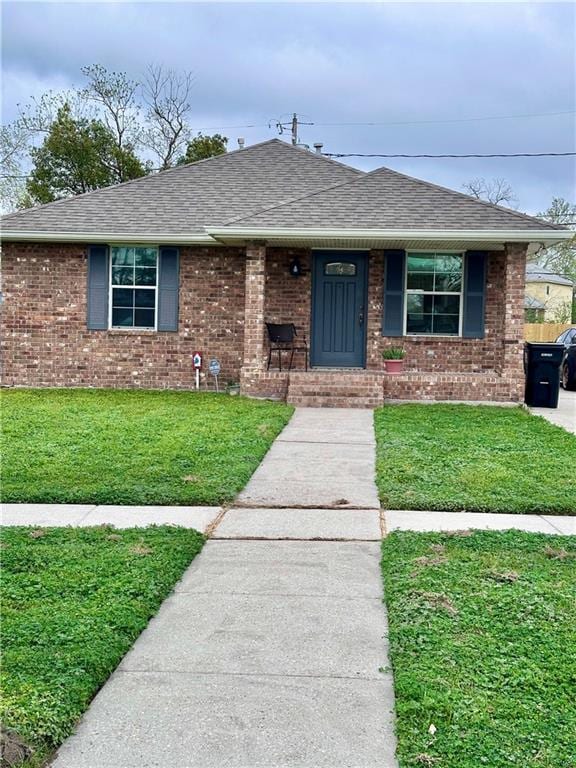 view of front of property with a front yard, brick siding, and roof with shingles