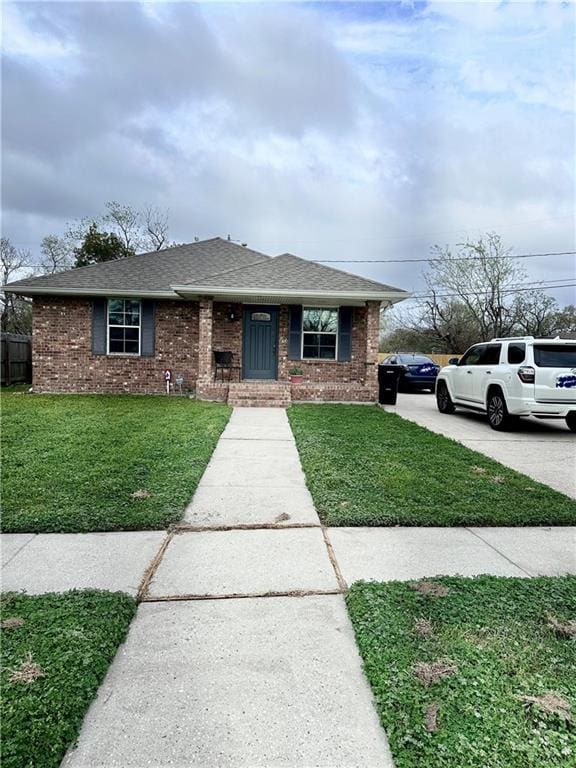 view of front of property with a front lawn, fence, roof with shingles, concrete driveway, and brick siding