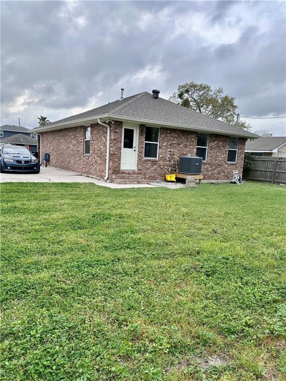 back of house with brick siding, a shingled roof, fence, central AC unit, and a yard