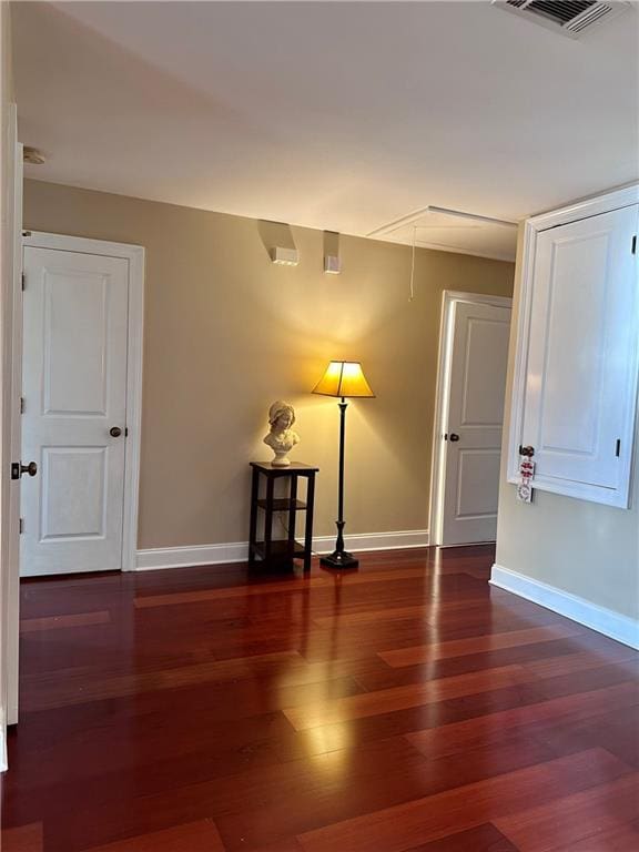 empty room with attic access, wood finished floors, visible vents, and baseboards