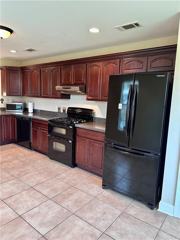 kitchen with light tile patterned floors, visible vents, black appliances, under cabinet range hood, and dark countertops