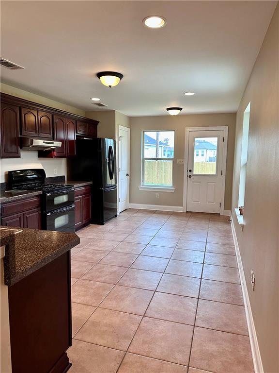 kitchen with dark brown cabinets, baseboards, under cabinet range hood, light tile patterned floors, and black appliances