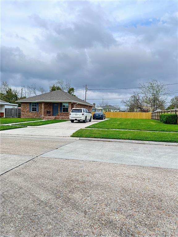view of front of home featuring brick siding, a front lawn, driveway, and fence