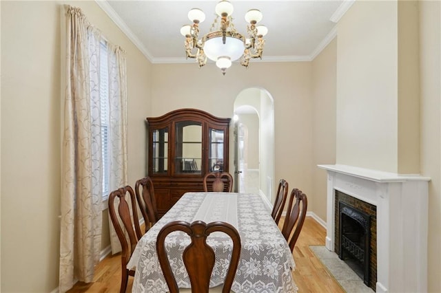 dining room featuring a chandelier, arched walkways, ornamental molding, and light wood-style flooring