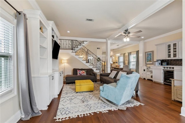 living area with beverage cooler, visible vents, dark wood finished floors, ornamental molding, and stairs