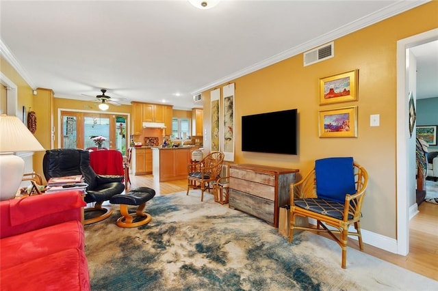 living room featuring baseboards, visible vents, ceiling fan, crown molding, and light wood-type flooring