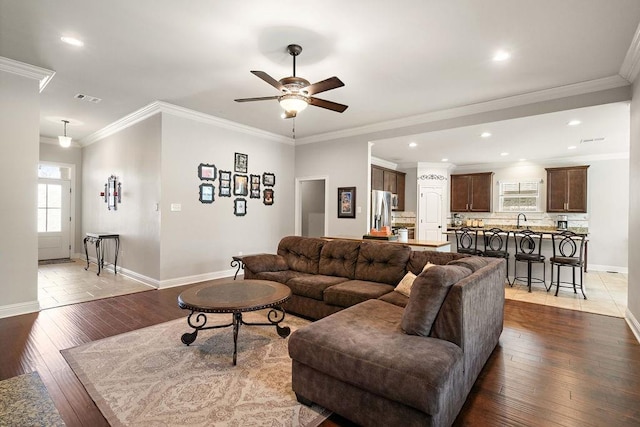 living area featuring visible vents, baseboards, ornamental molding, a ceiling fan, and wood-type flooring