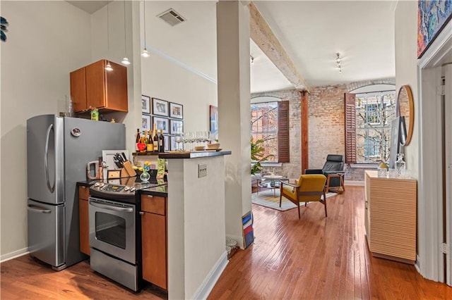 kitchen featuring visible vents, dark countertops, hardwood / wood-style floors, appliances with stainless steel finishes, and brick wall